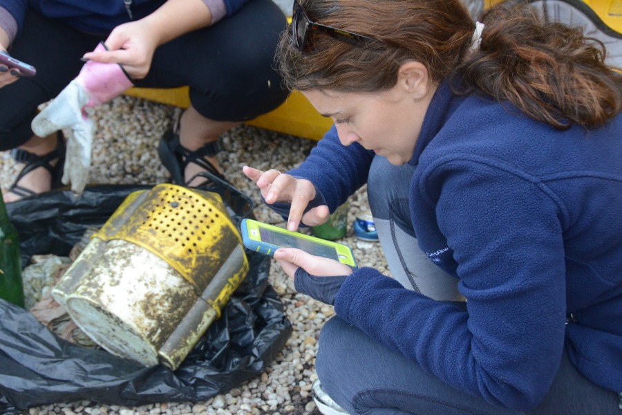 A woman crouching above a large piece of trash logs debris data into the Litter-Free Digital Journal during a litter sweep with the South Carolina Aquarium